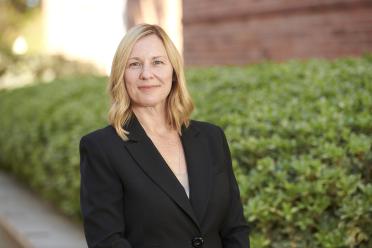 Photograph of Amander Clark, PhD wearing a black suit jacket and standing in front of greenery. 