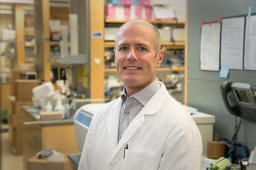 Headshot of S. Thomas Carmichael in a lab coat smiles in a UCLA lab