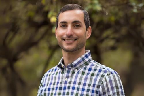 A man smiles at the camera while standing outdoors.