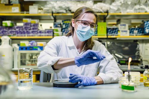 A masked UCLA researcher works before a small open flame in a laboratory. 