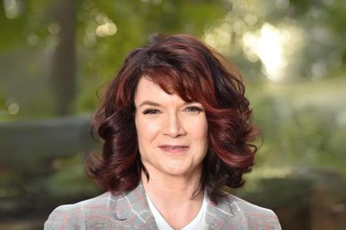 A woman smiles into the camera while standing outdoors.