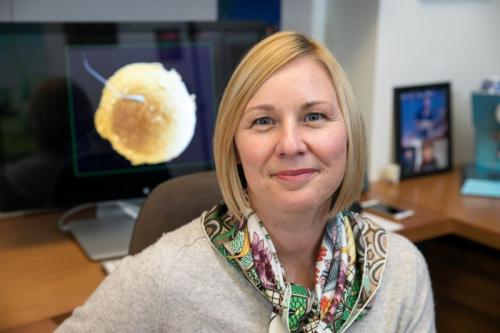 Researcher Amander Clark smiles at her desk, wearing a brightly colored scarf.