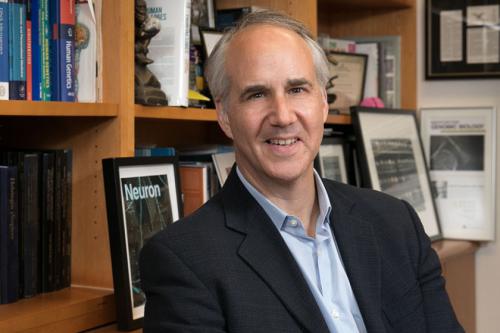 Researcher Daniel Geschwind smiles in his office before a bookshelf.