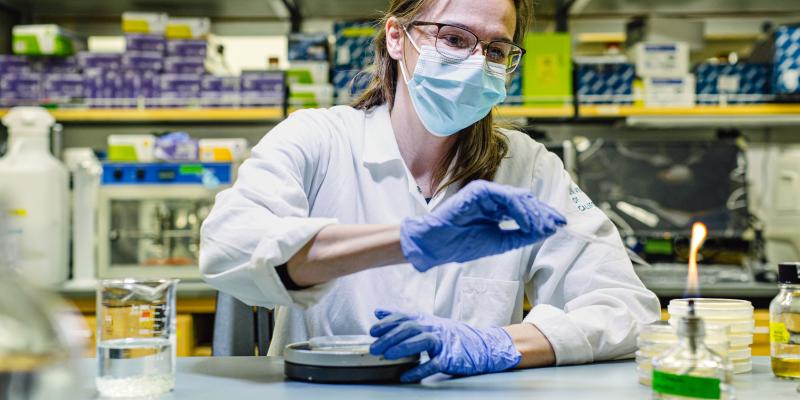 A masked UCLA researcher works before a small open flame in a laboratory. 