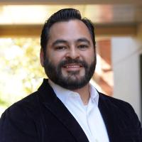 Male researcher with short dark hair wearing a white shirt and a black jacket.