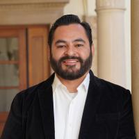 Male researcher with dark hair wearing a black blazer and a white shirt. 